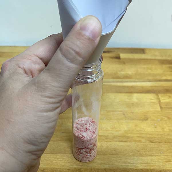 Using paper funnel to fill tube with crushed candy cane